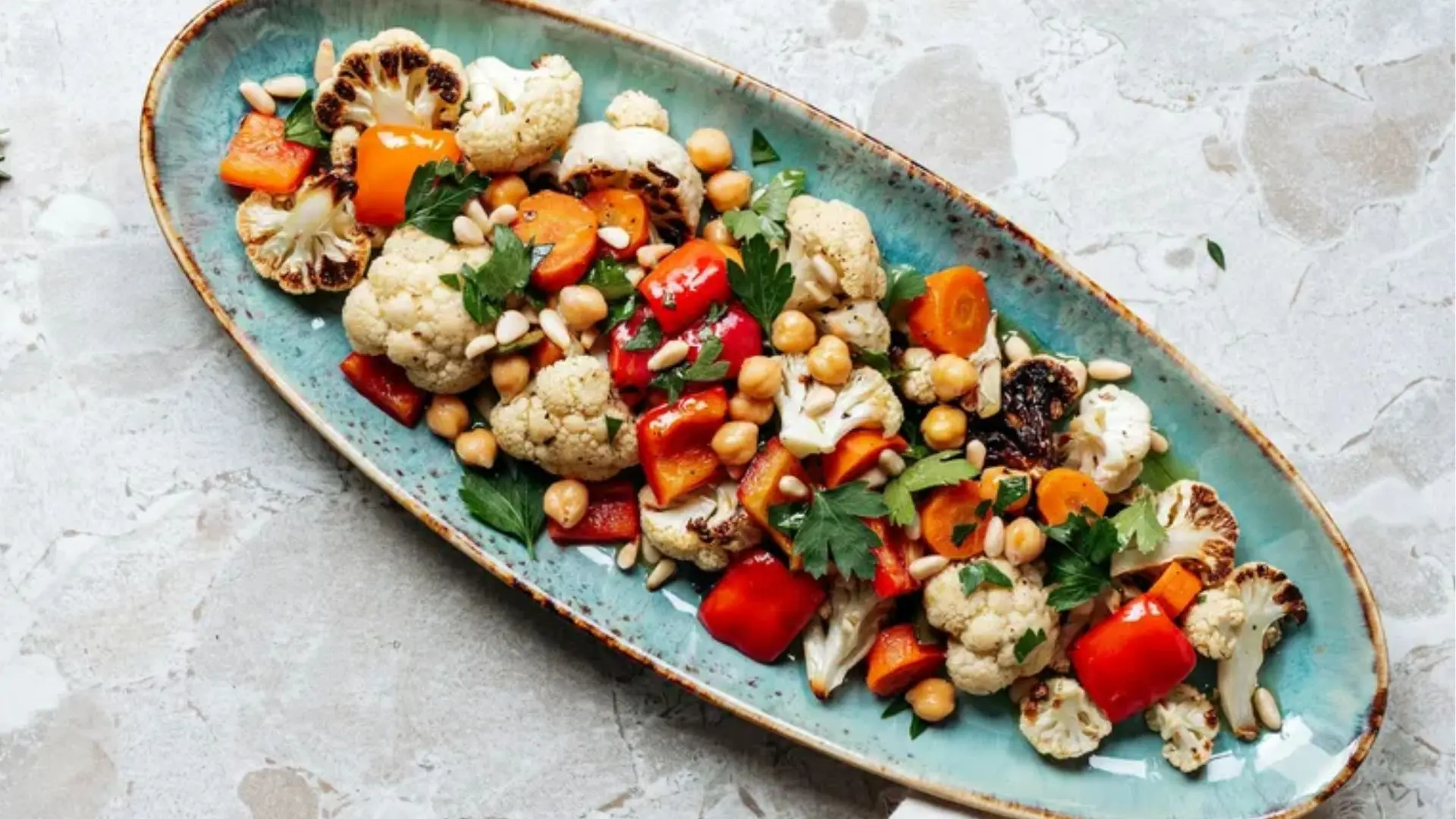 A serving plate of assorted vegetables accompanied by a stainless steel spoon.