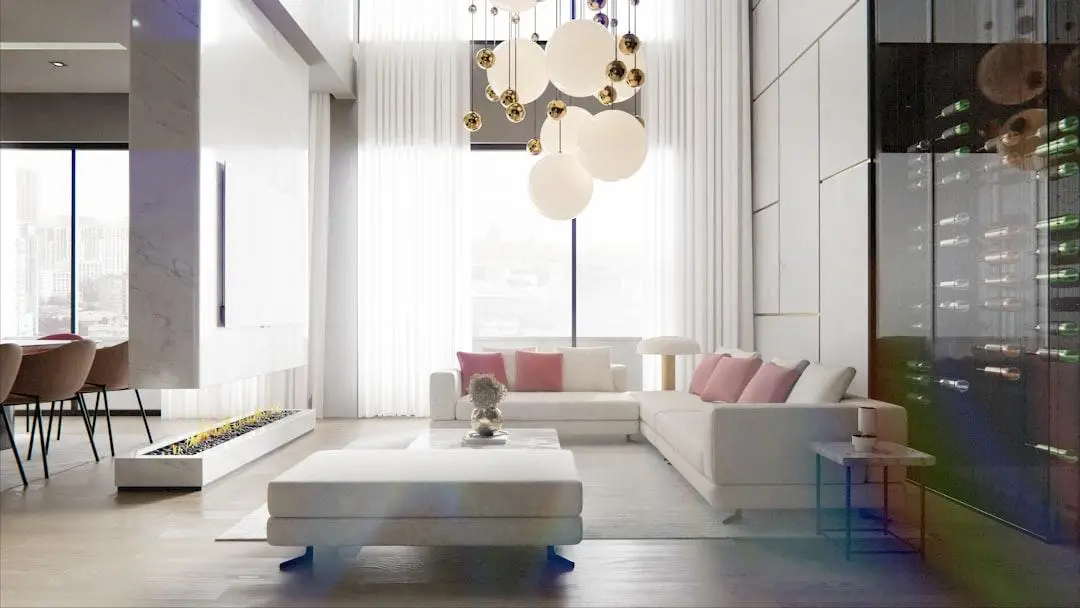 Modern living room with white sofas, gold-accented chandelier, and wine storage wall under bright daylight