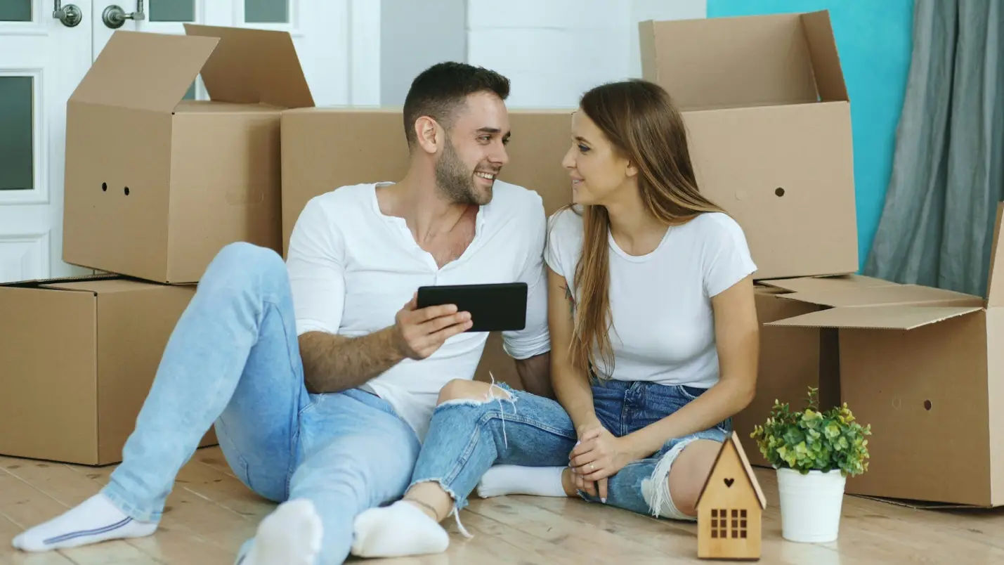 Couple sitting on floor with tablet among cardboard boxes in bright room
