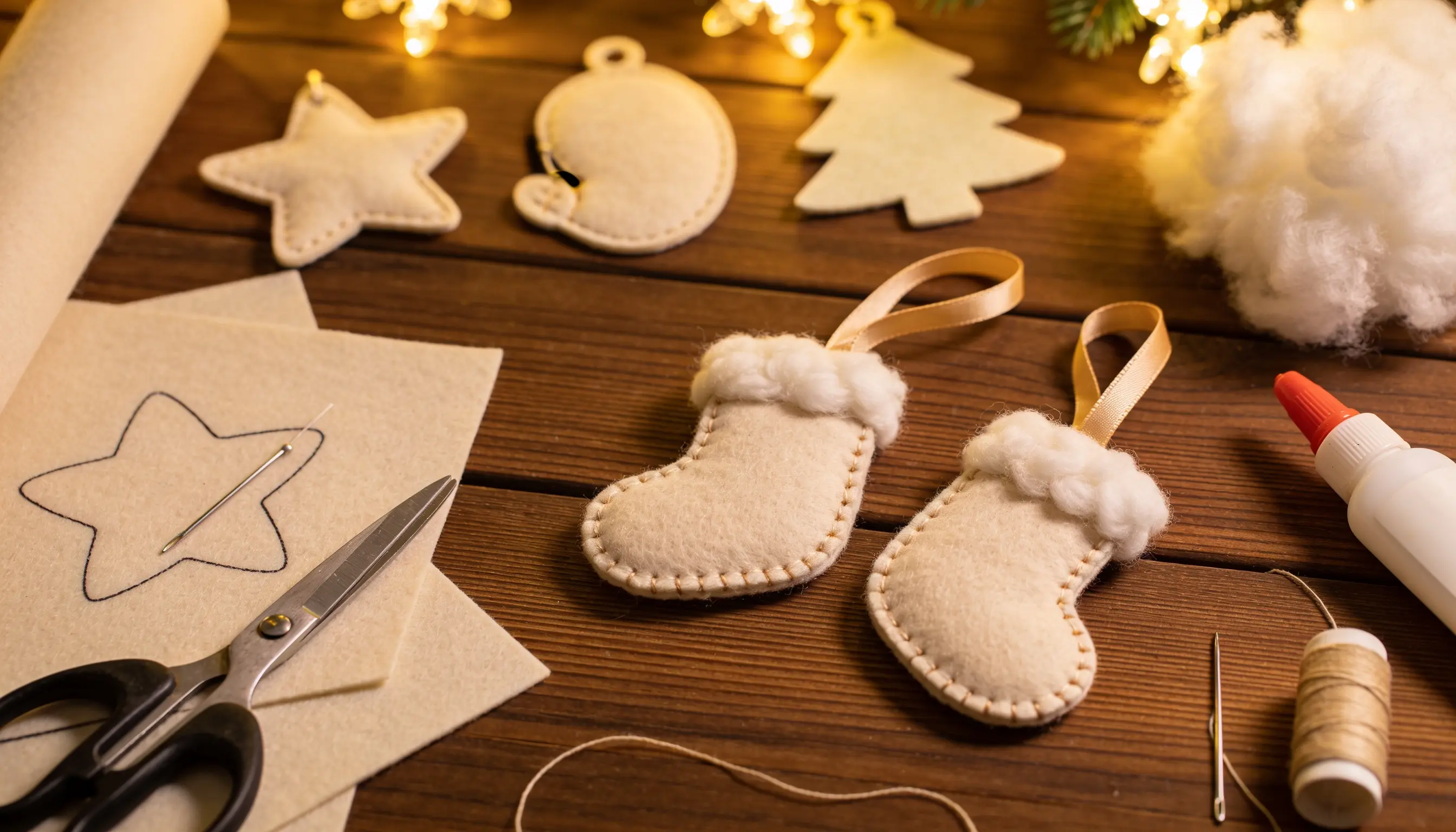 Handmade felt Christmas ornaments in progress, including stockings, stars, and a tree, with craft supplies on a wooden table.