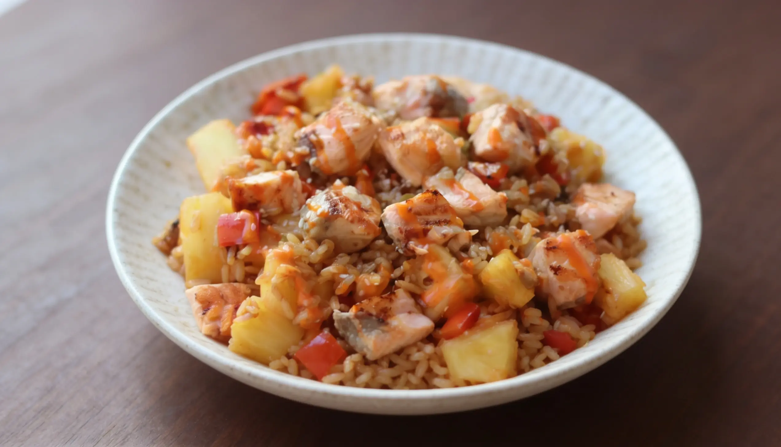 Bowl of salmon, rice, pineapple, and red pepper filled with sauce.