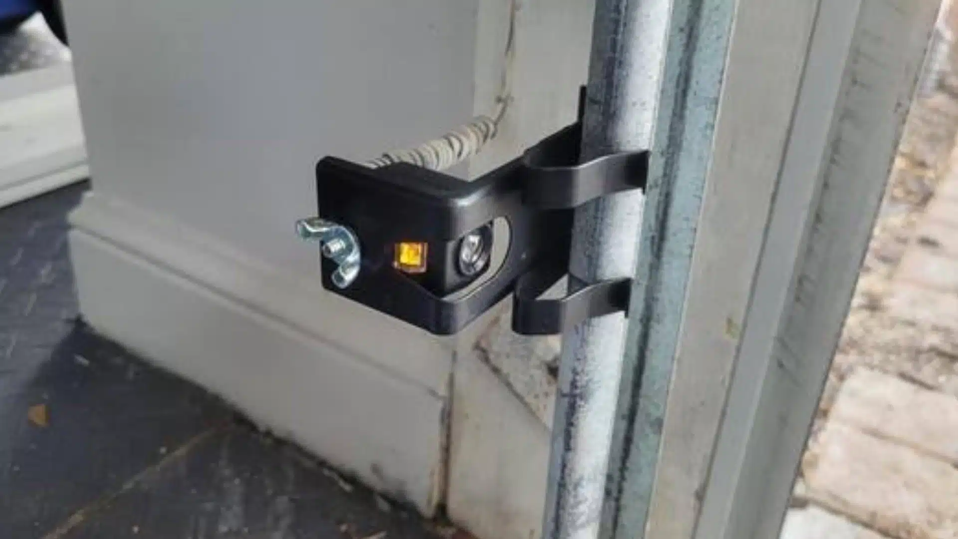 Garage door safety sensor mounted on the track with an amber indicator light showing power before alignment testing