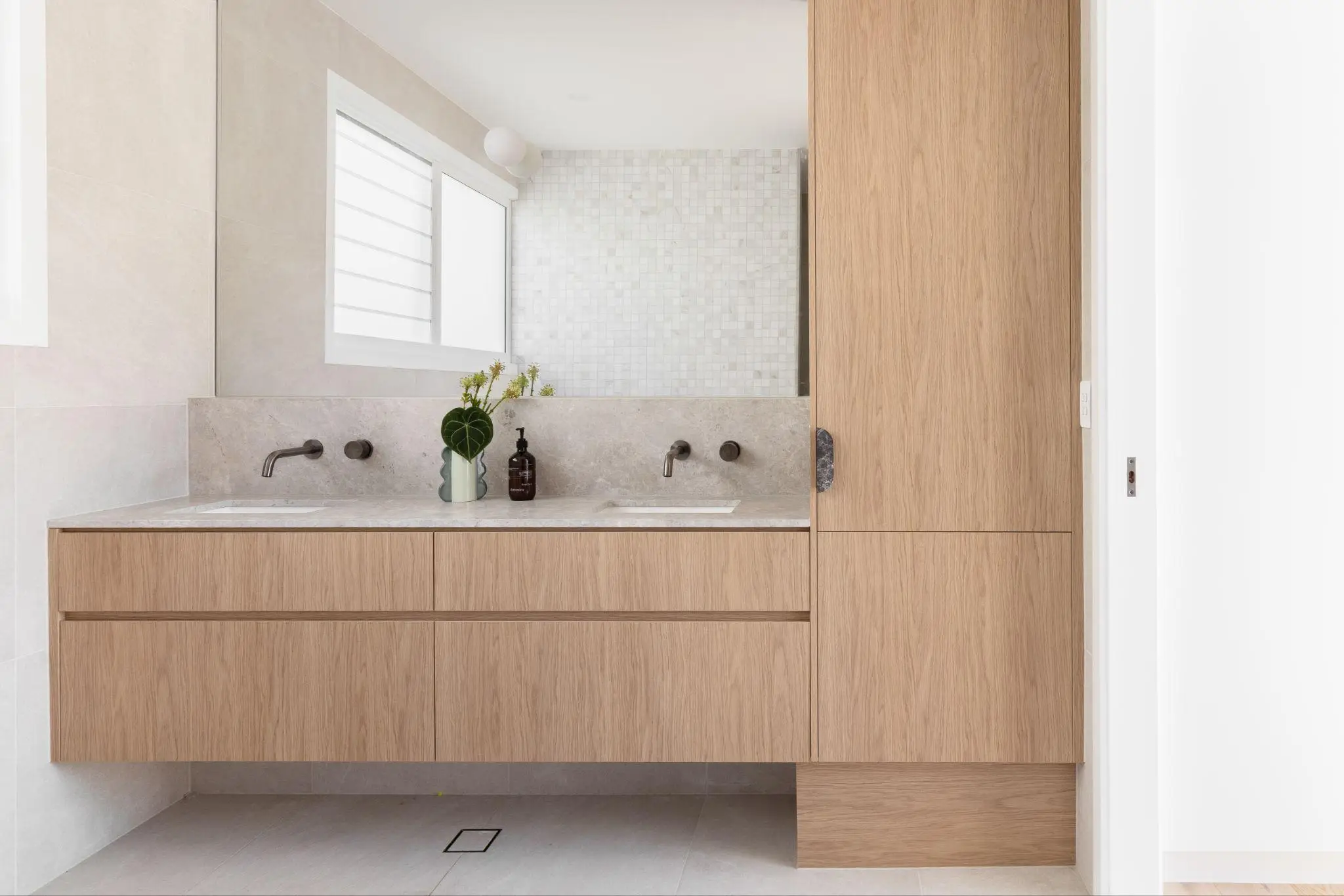 Contemporary bathroom with wooden vanity, double sink, and decorative plants under natural light