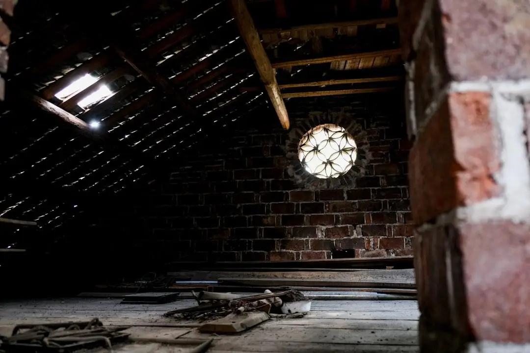 Dimly lit attic with brick walls and circular window, scattered wooden boards on the floor