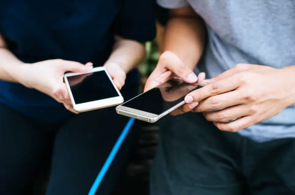 Two people holding smartphones outdoors, sharing information through screen interaction