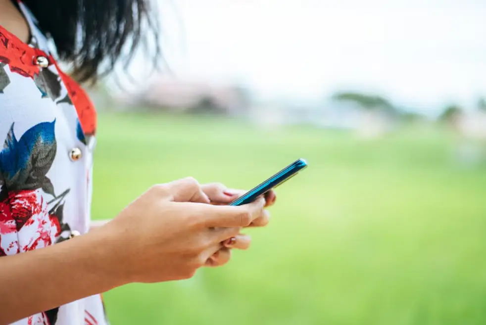 Person using smartphone outdoors with green blurred background