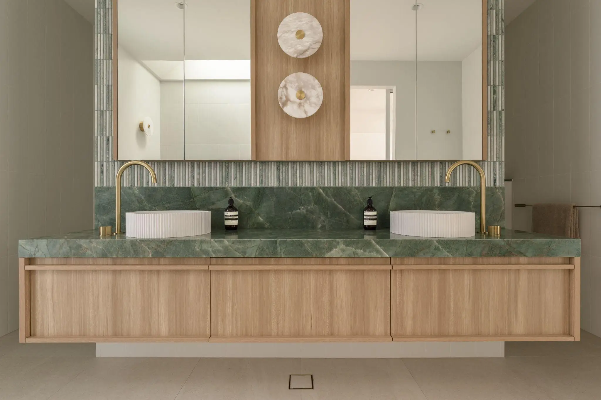Modern bathroom with green marble countertop, dual sinks, gold faucets, and wooden cabinetry