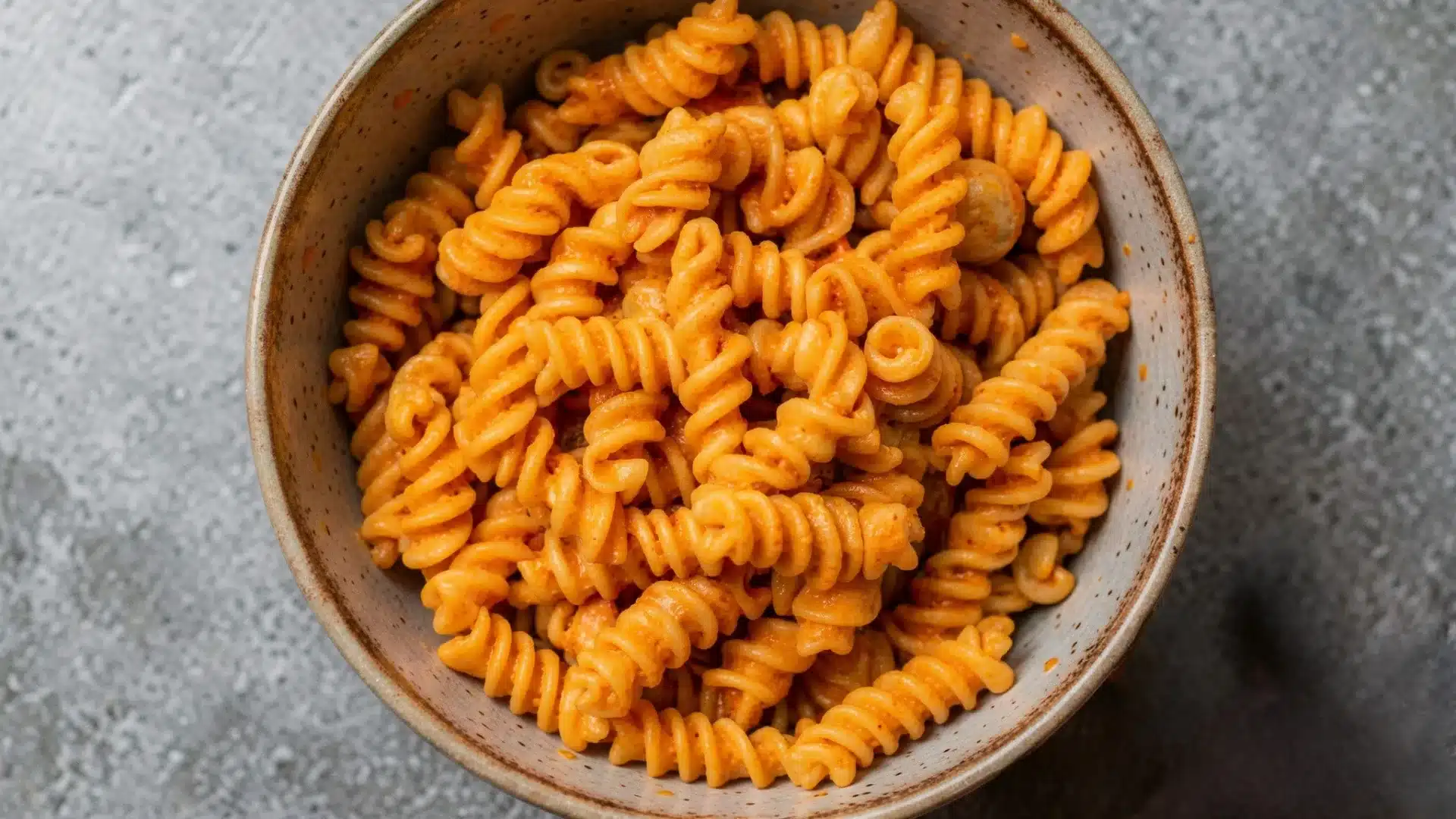 A bowl of pot pasta topped with melted cheese, garnished with herbs, set on a wooden table