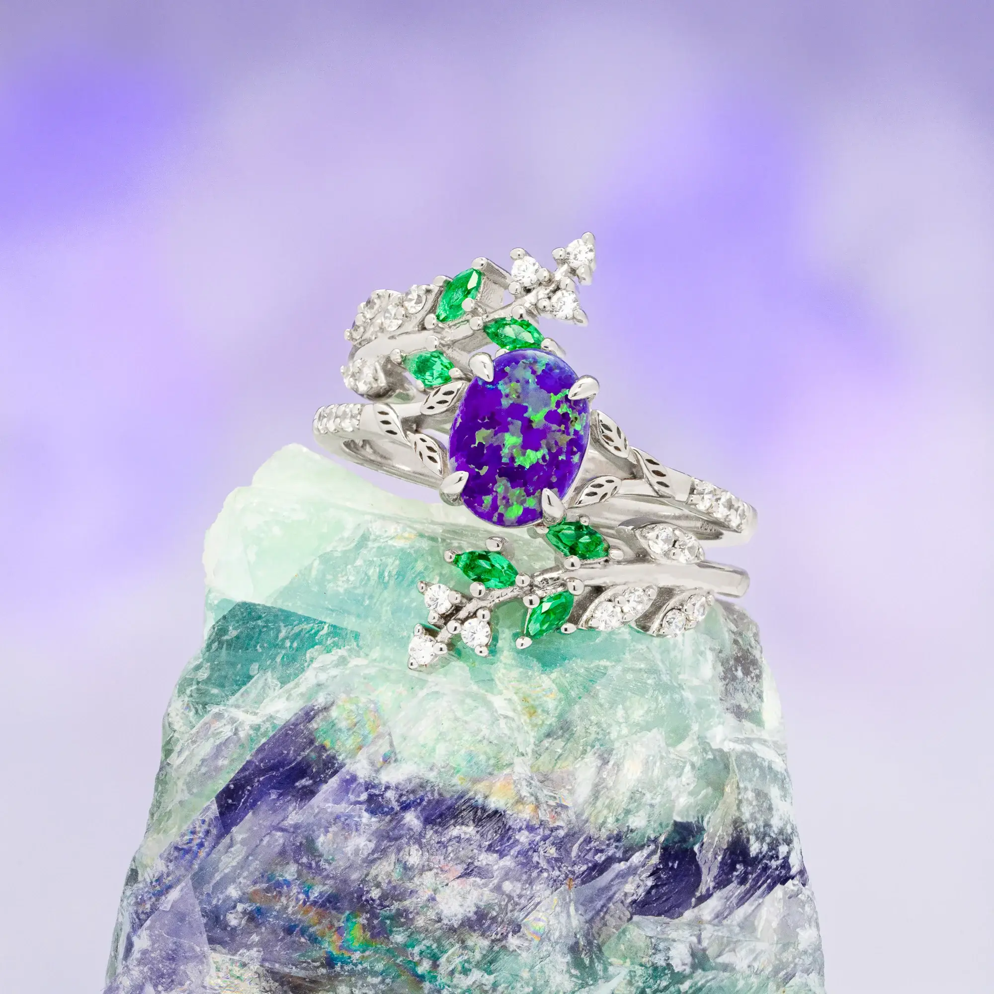 Intricately designed silver ring with purple opal and green gemstones on crystal backdrop