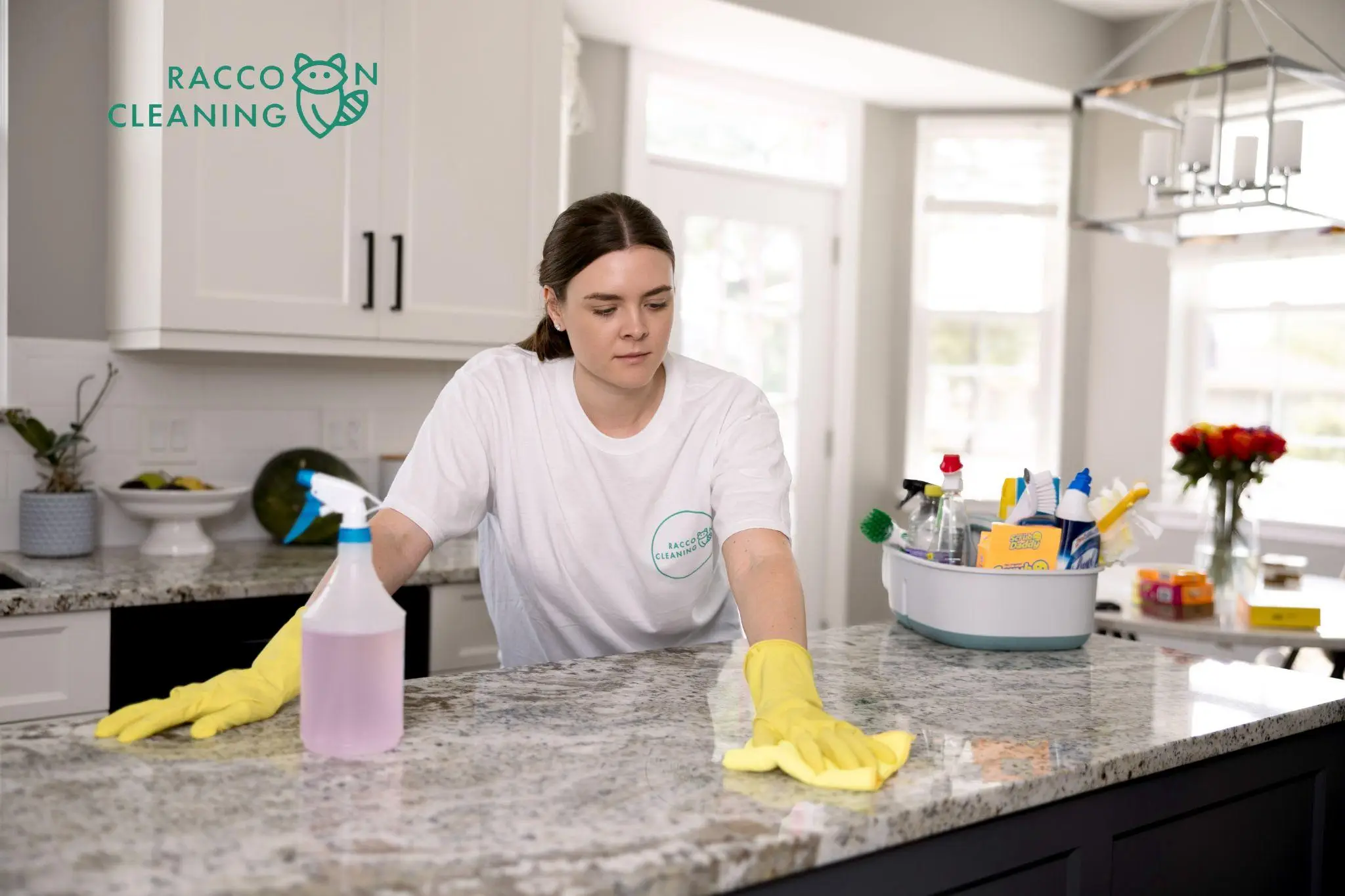 Person cleaning granite kitchen counter with yellow gloves and cleaning spray, bright natural light