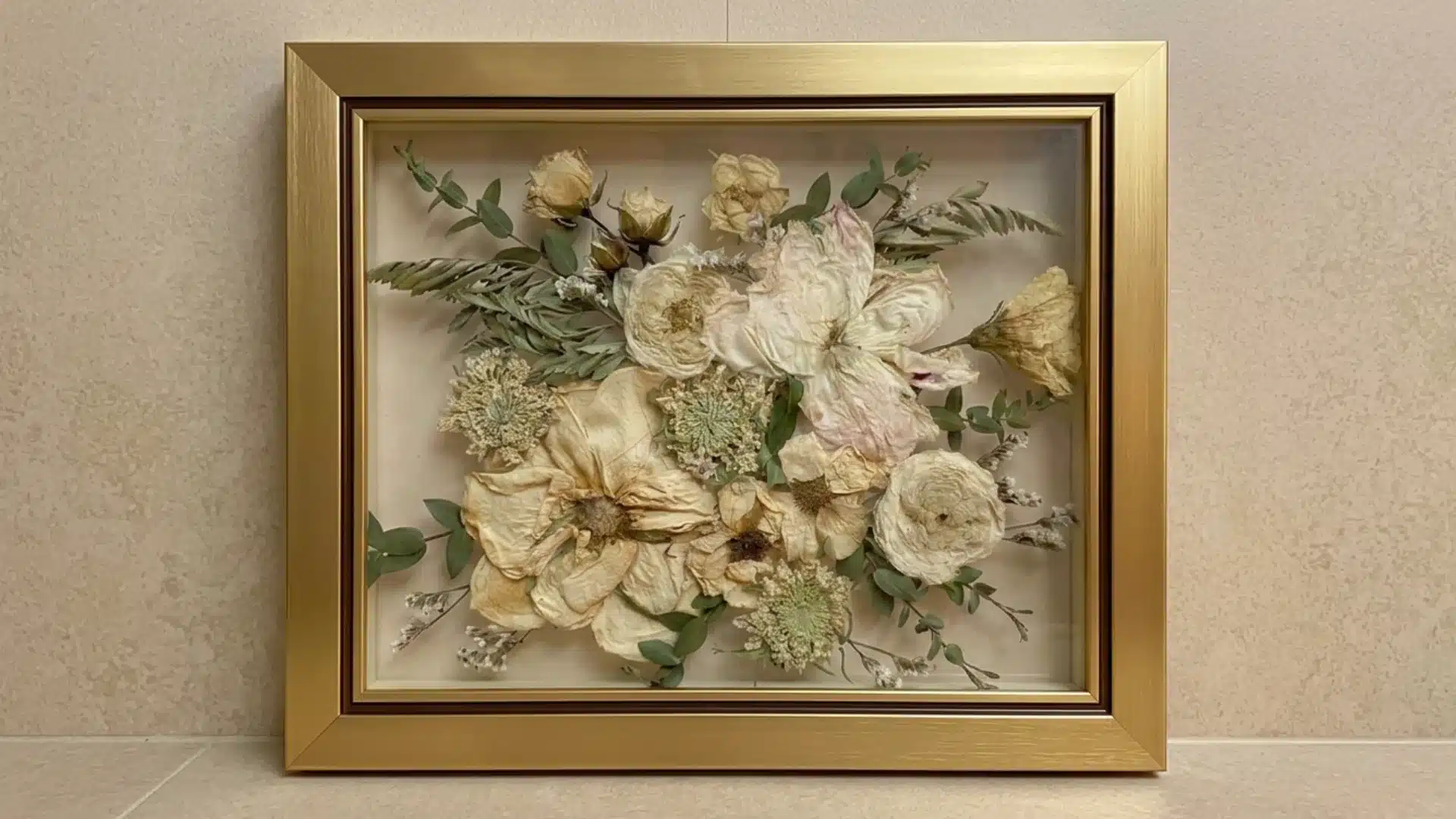 Dried wedding bouquet preserved in a gold frame with pressed flowers and greenery.