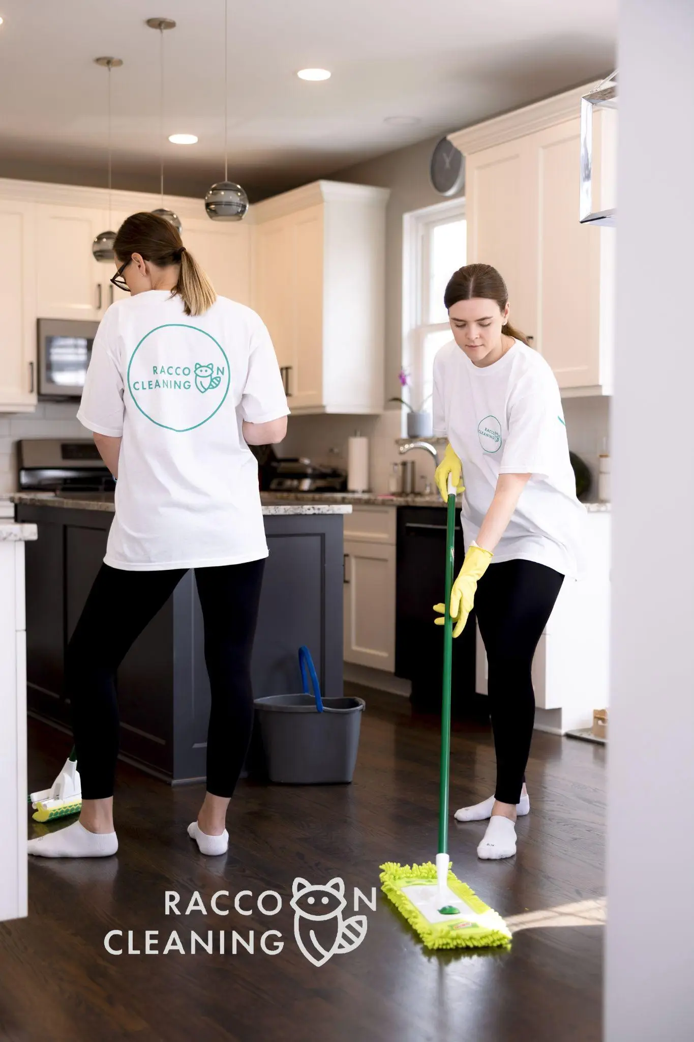 Two people mopping floor in bright kitchen wearing white cleaning uniforms