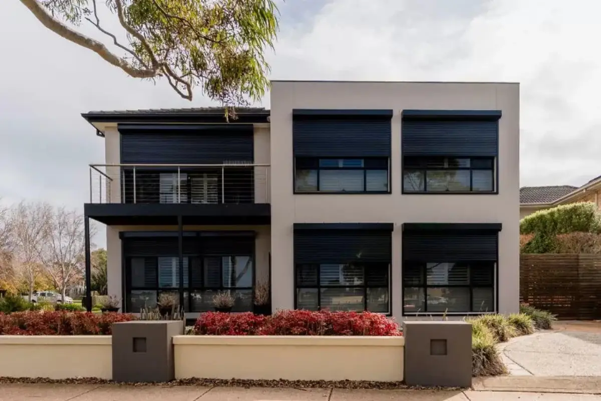 Modern two-story house with large dark windows and red shrubs in the front yard
