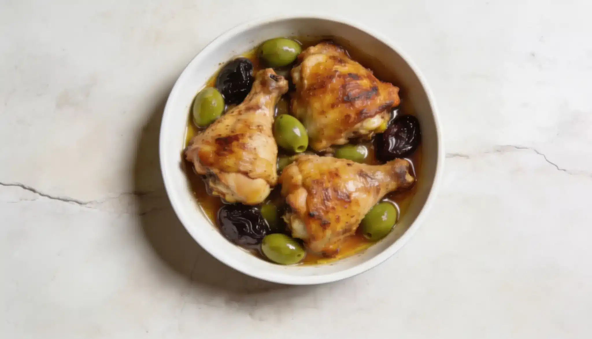A bowl filled with chicken pieces and olives placed on a wooden table.