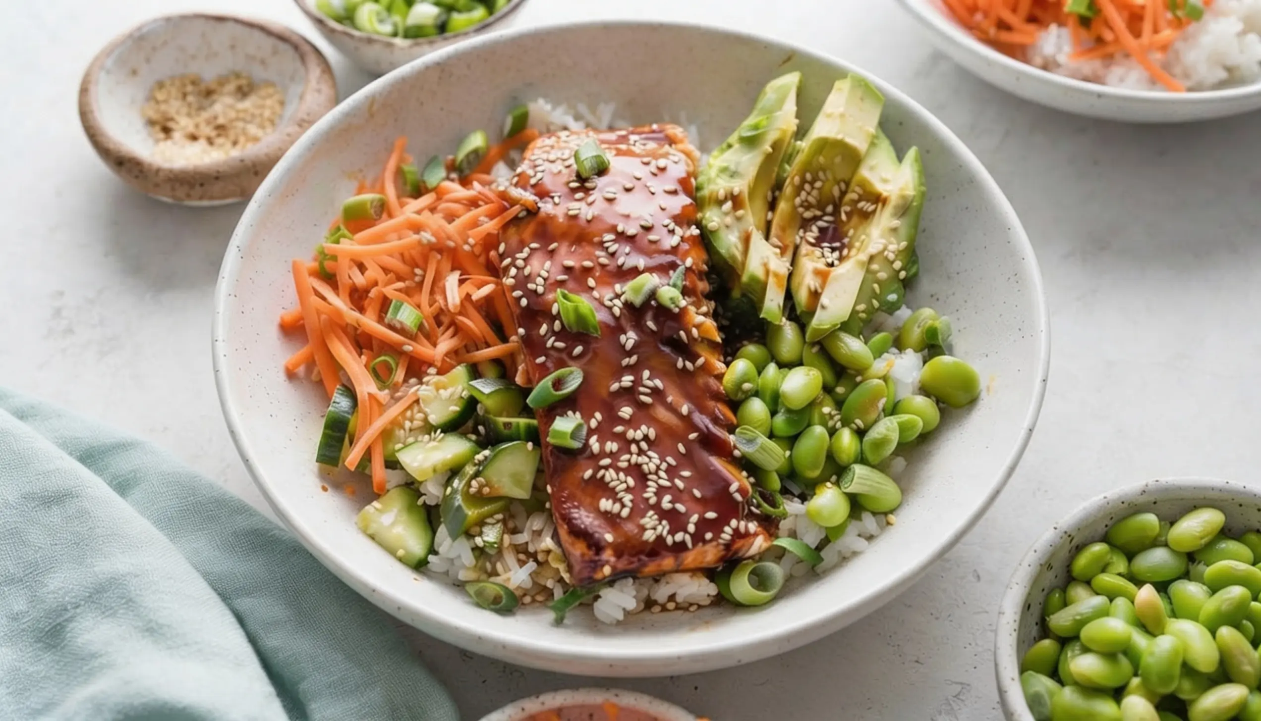 Salmon poke bowl with rice, avocado, edamame, cucumber, and shredded carrots, garnished with sesame seeds and green onions.