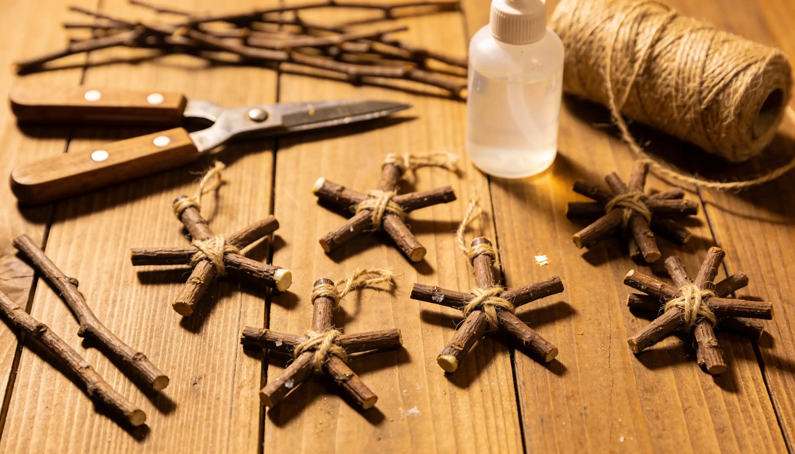 Crafting rustic twig ornaments with twine, scissors, and glue on a wooden surface.
