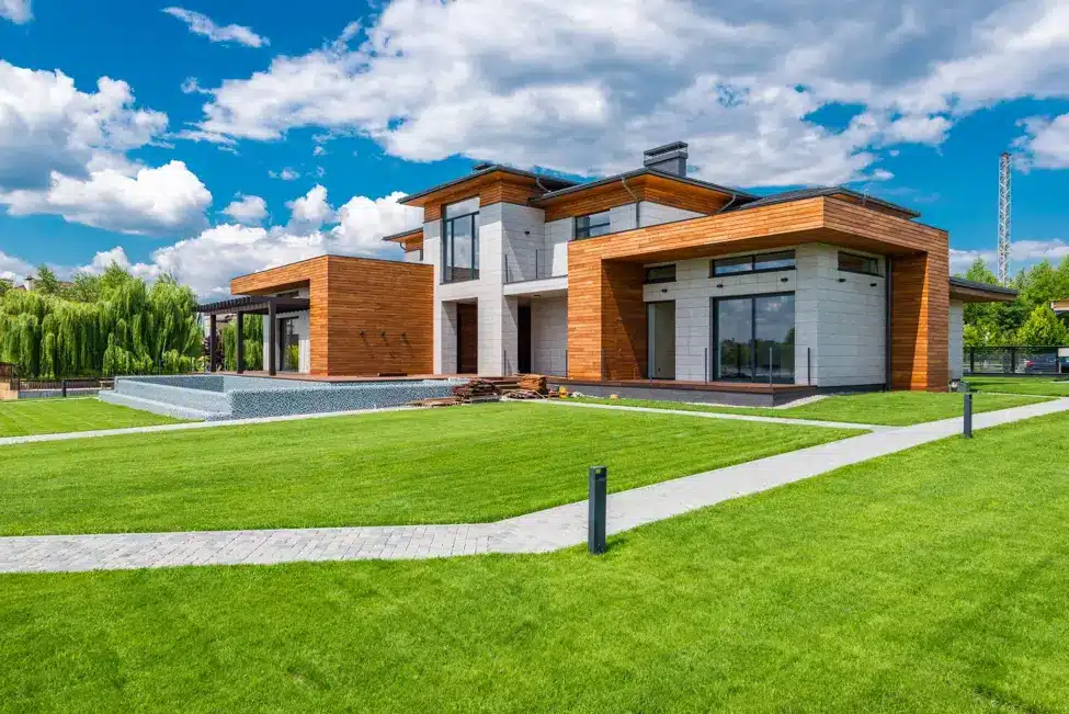 Modern house with wooden paneling and large windows on landscaped lawn under blue sky