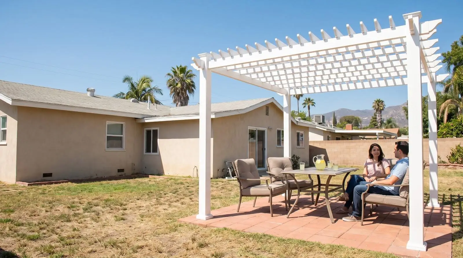 Couple sitting under white pergola in sunny backyard with patio furniture and lemonade pitcher