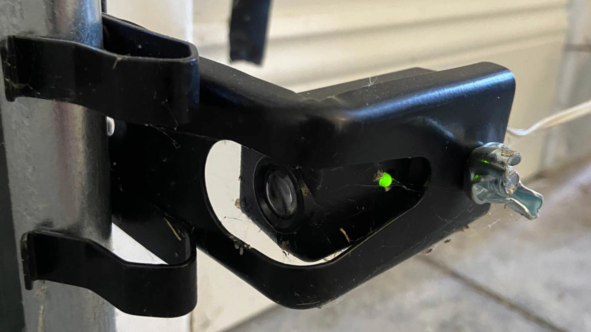 Garage door safety sensor with glowing green LED showing alignment issues and dust buildup on the sensor housing