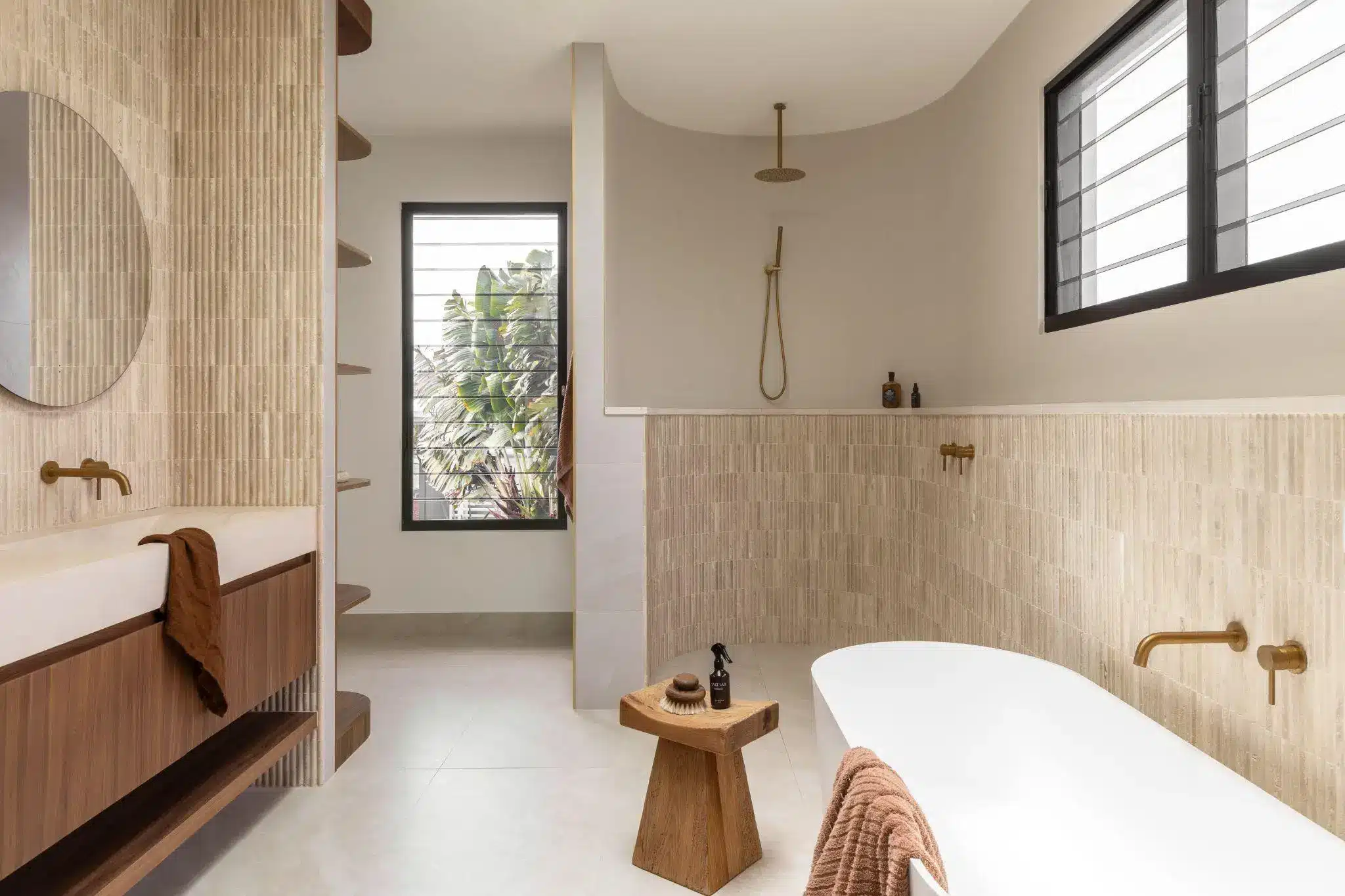Modern bathroom with freestanding tub, wood accents, round mirror, and natural light streaming in