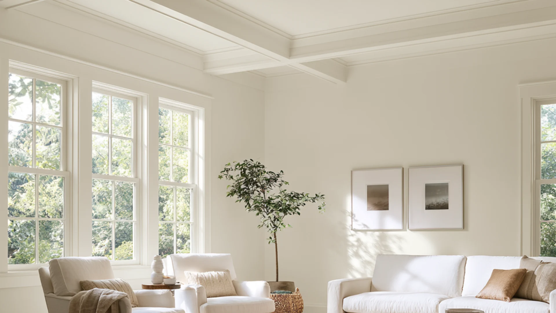A bright living room featuring white furniture and large windows allowing natural light to fill the space.