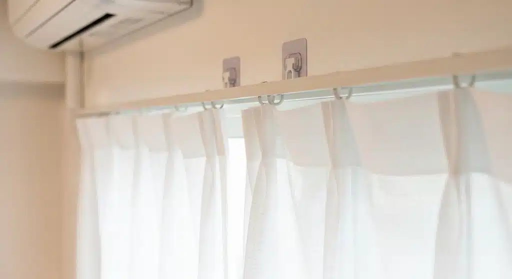 Adhesive hooks supporting a lightweight curtain rod and white sheer curtains for a simple no-drill window treatment.