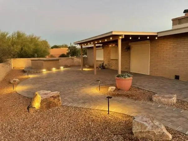 Covered patio with string lights in a landscaped backyard featuring paving stones and desert plants