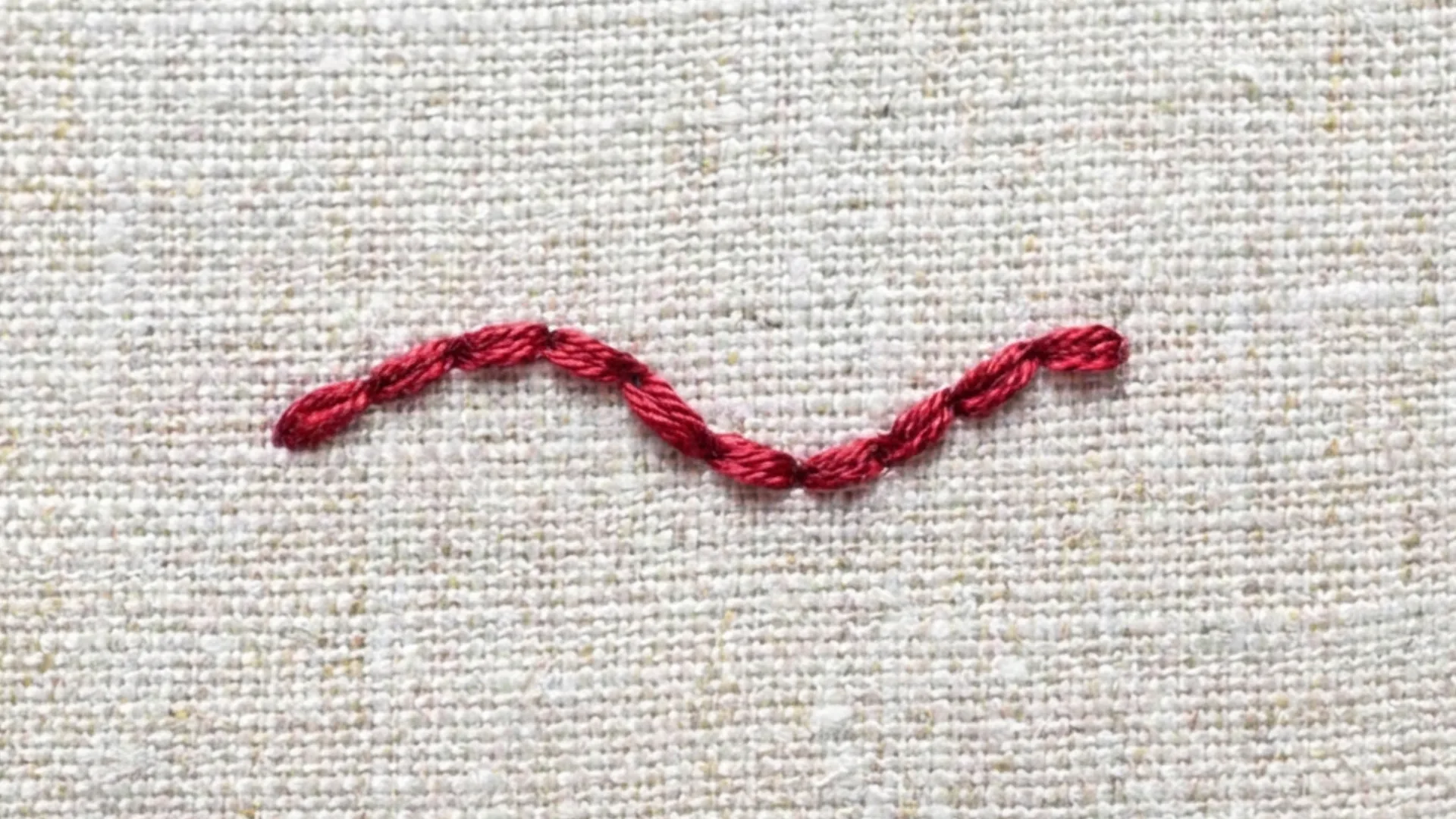 Backstitch in red thread forming a curved connected line across textured white fabric in a simple embroidery sample