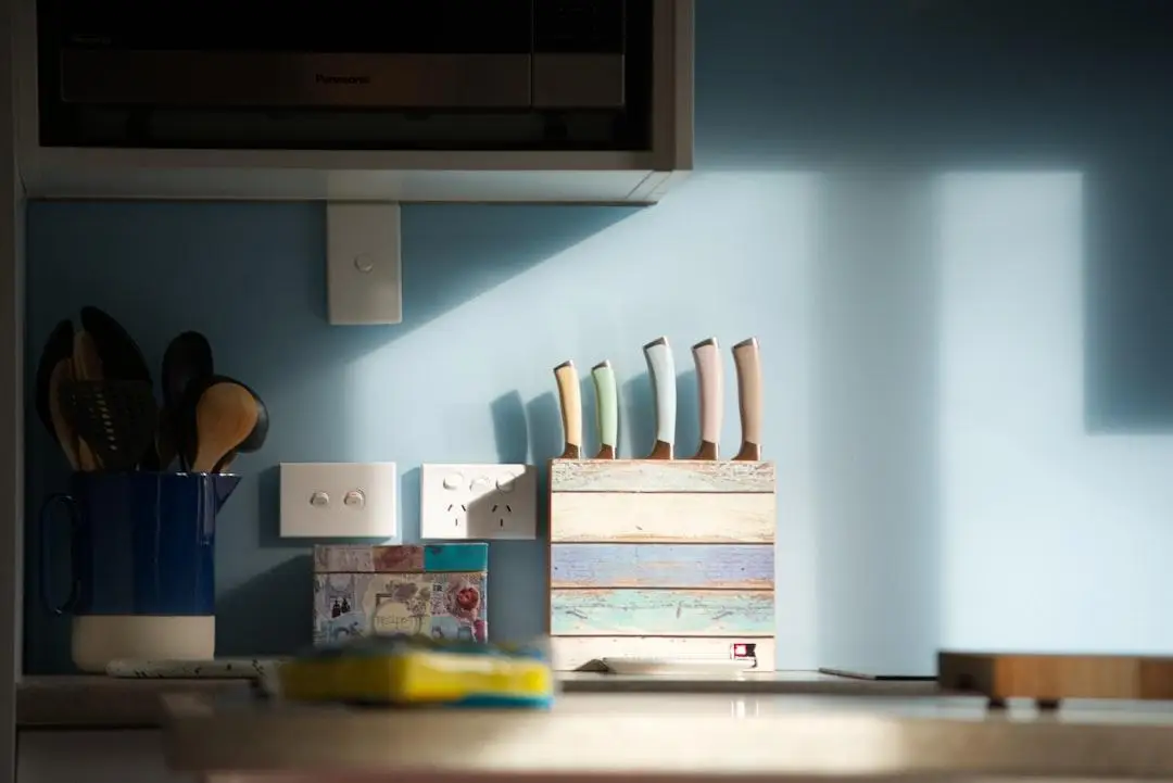 Knife block and utensil holder on kitchen countertop against blue wall in natural light