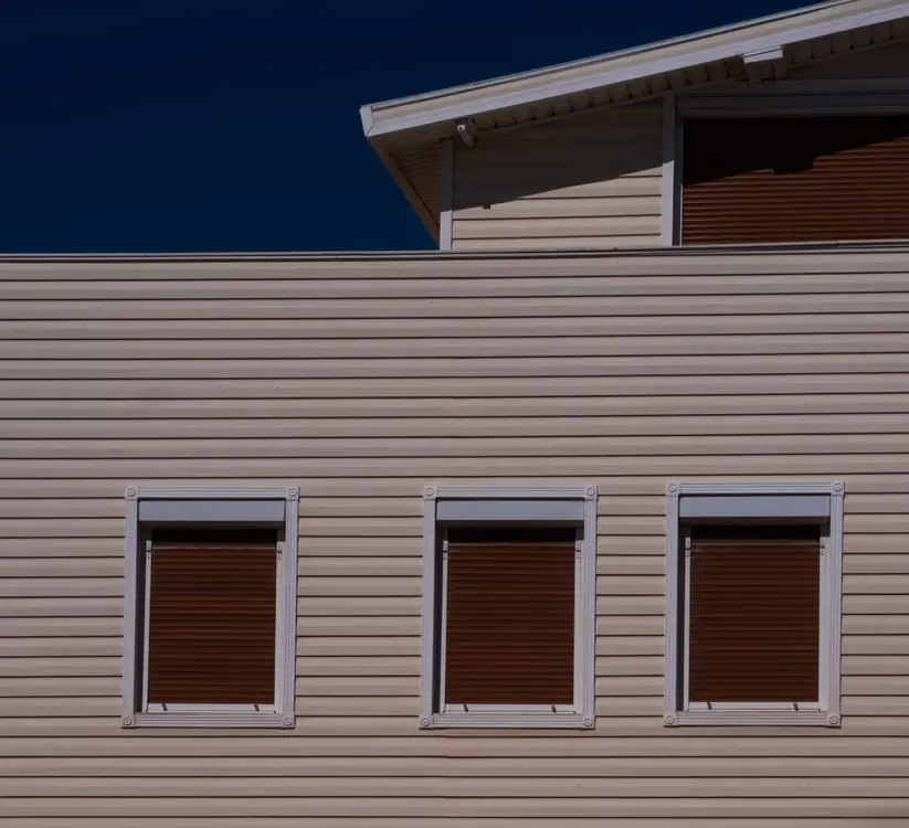 Cream-colored building exterior with three closed brown shutters and deep blue sky above