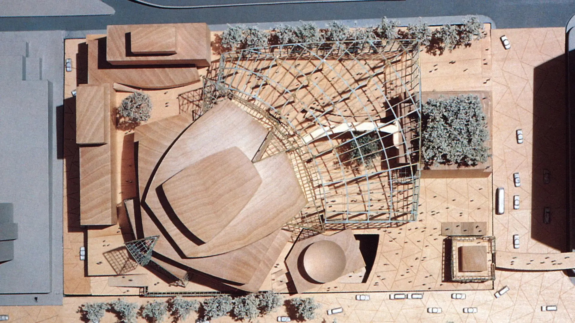 overhead architectural model showing curved concert hall volumes lattice structures plazas trees and surrounding roads