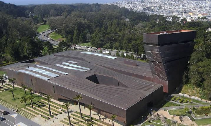 contemporary cultural building with a broad cantilevered roof overlooking a green lawn and palm trees