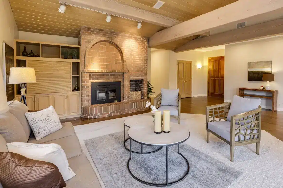 Cozy living room with brick fireplace, gray sofa, and round coffee tables on a plush rug
