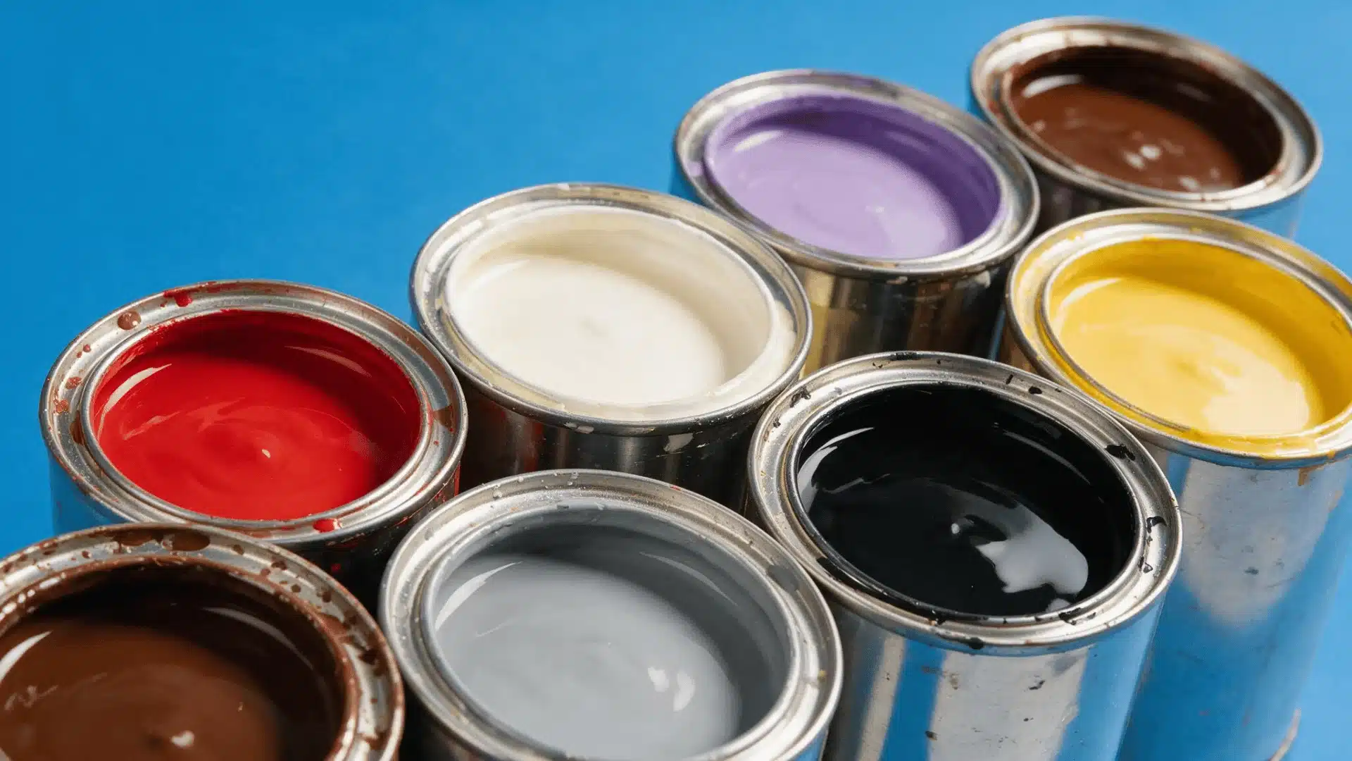 Overhead view of open metal paint cans with colorful paint on a blue background.