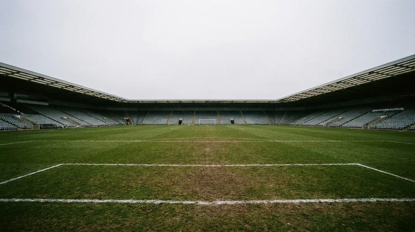 Empty football stadium with green field and seating under overcast sky