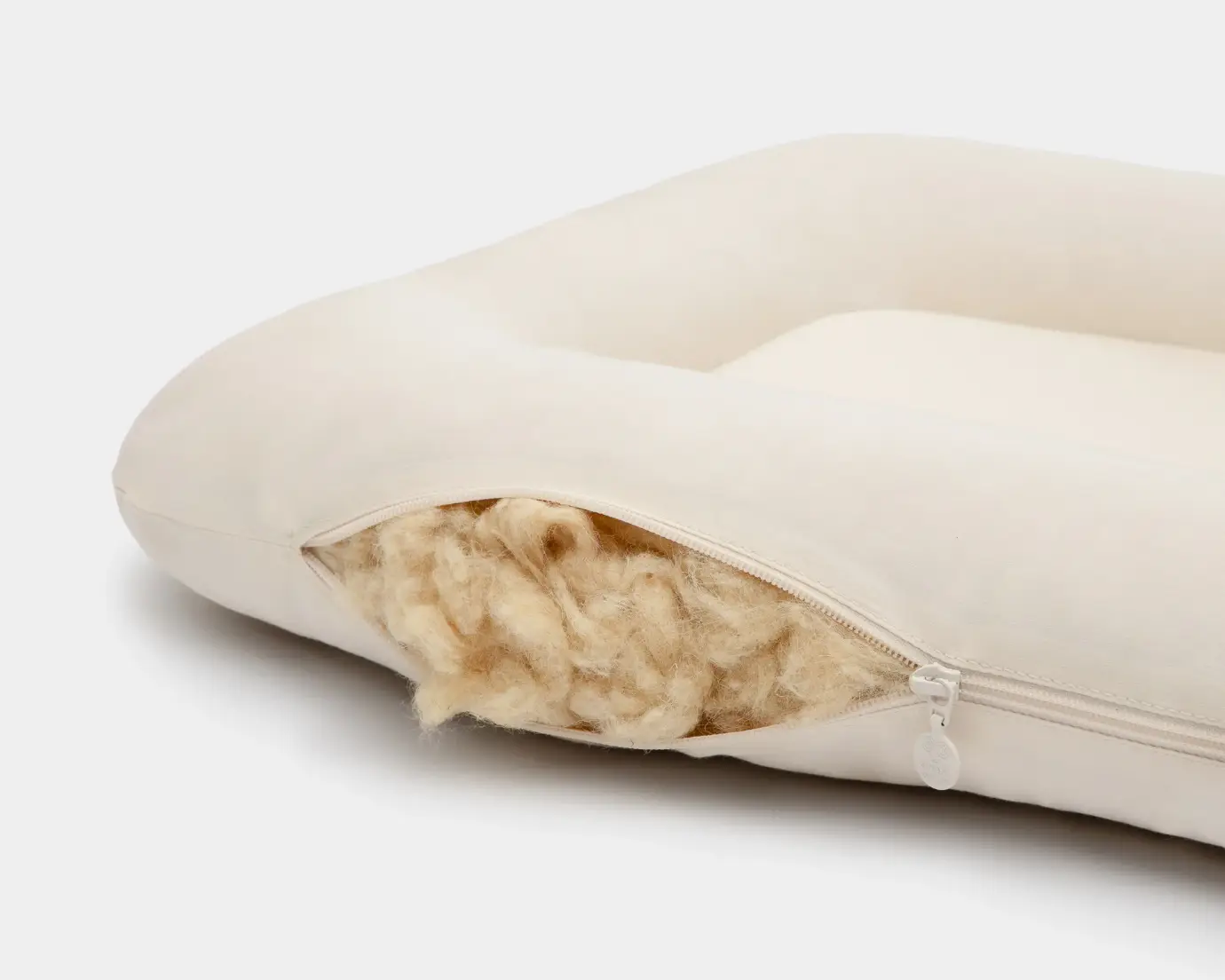 Partially opened white cushion with visible wool filling on a plain background