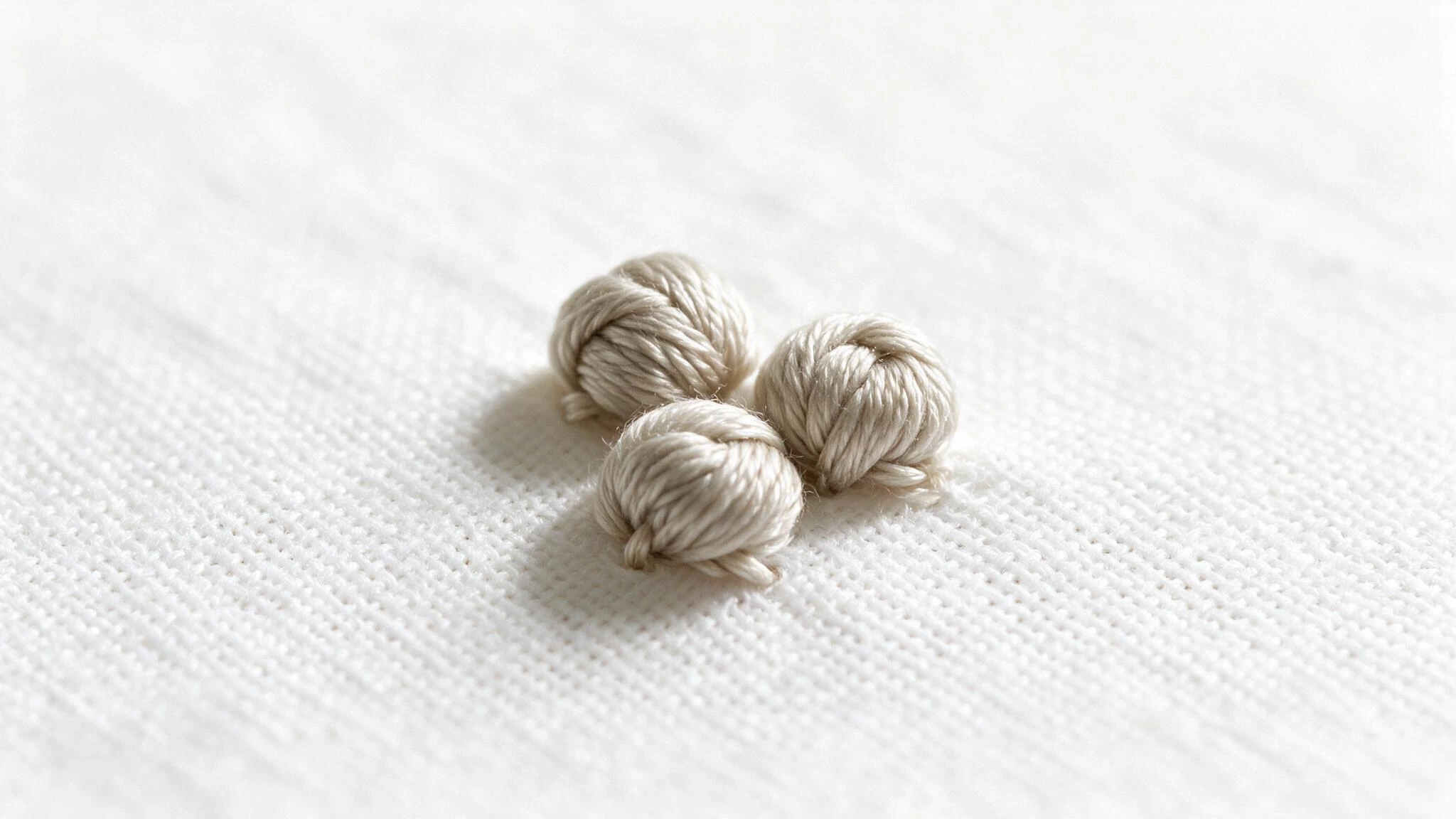 French knot stitch in beige thread forming three raised rounded knots on white fabric in a simple embroidery sample
