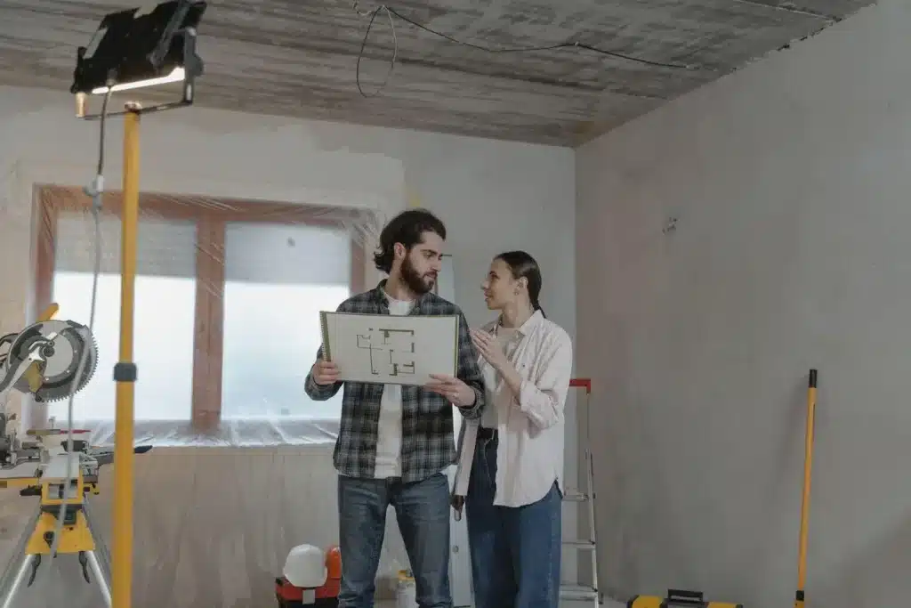 Two people discussing floor plans in a partially renovated room with tools and ladder present
