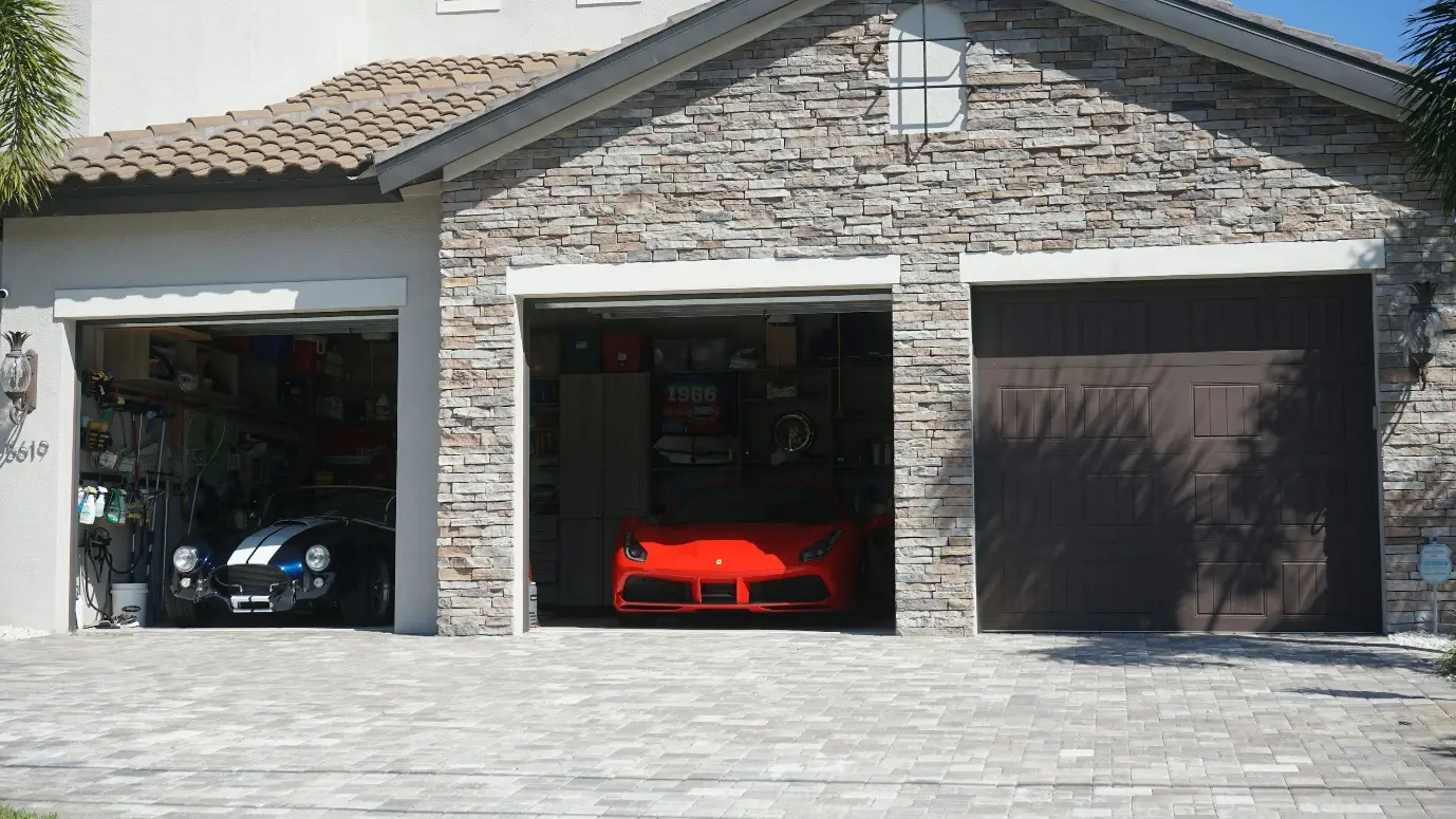Two sport cars in a stone garage with open doors and tiled driveway