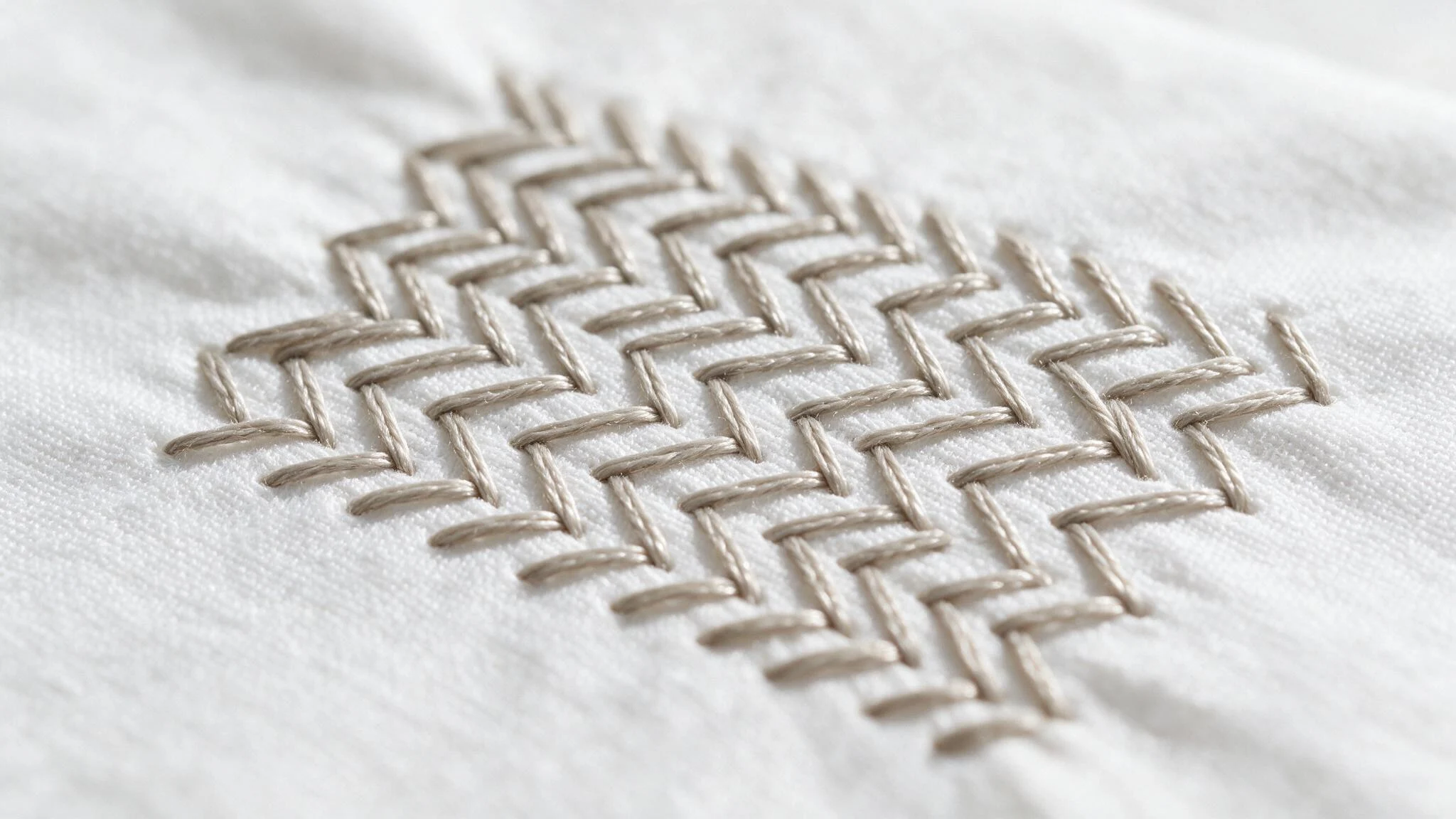 Herringbone stitch in beige thread forming a neat crossed geometric pattern across softly wrinkled white fabric