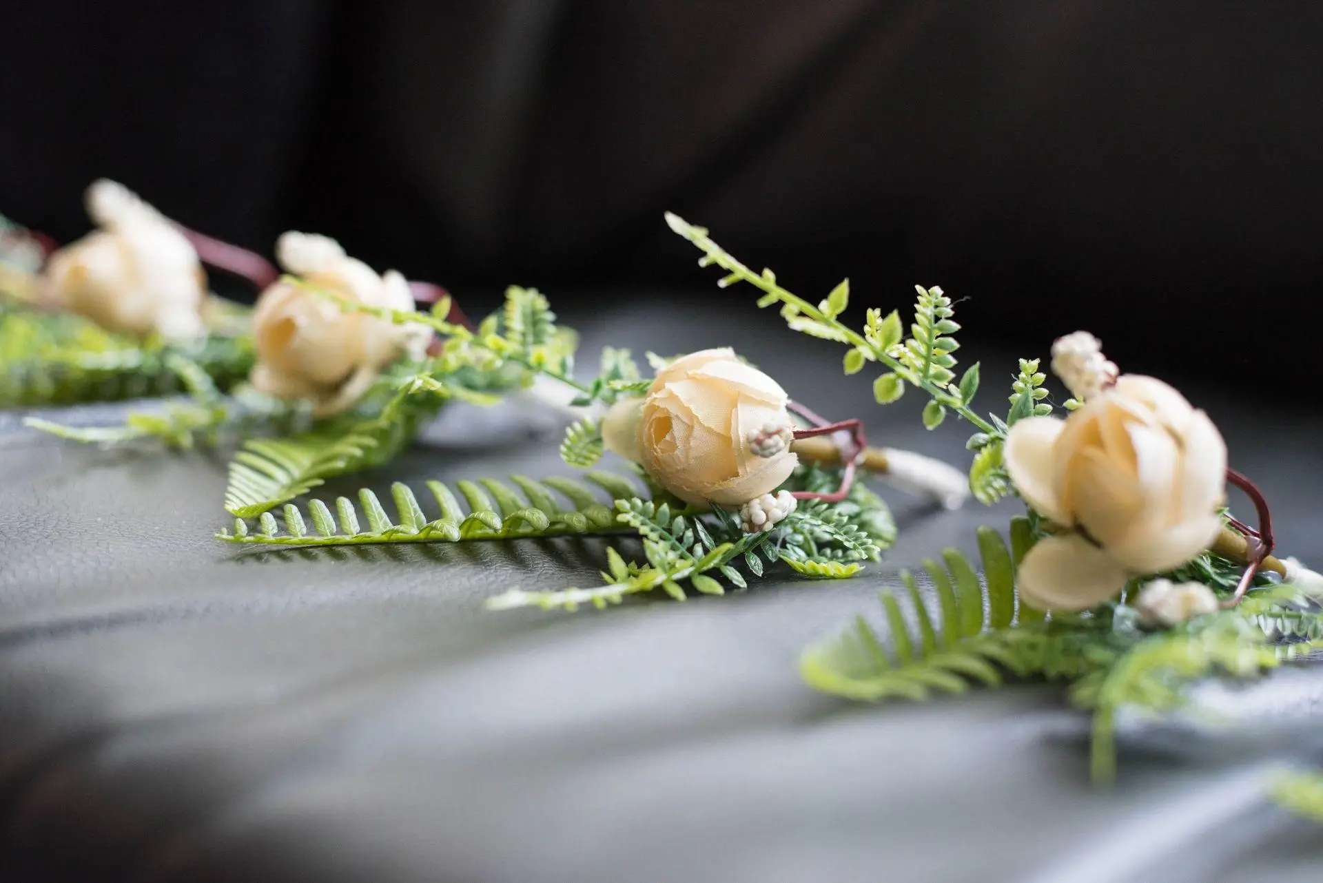 Cream-colored artificial flowers and green ferns arranged on dark textured surface