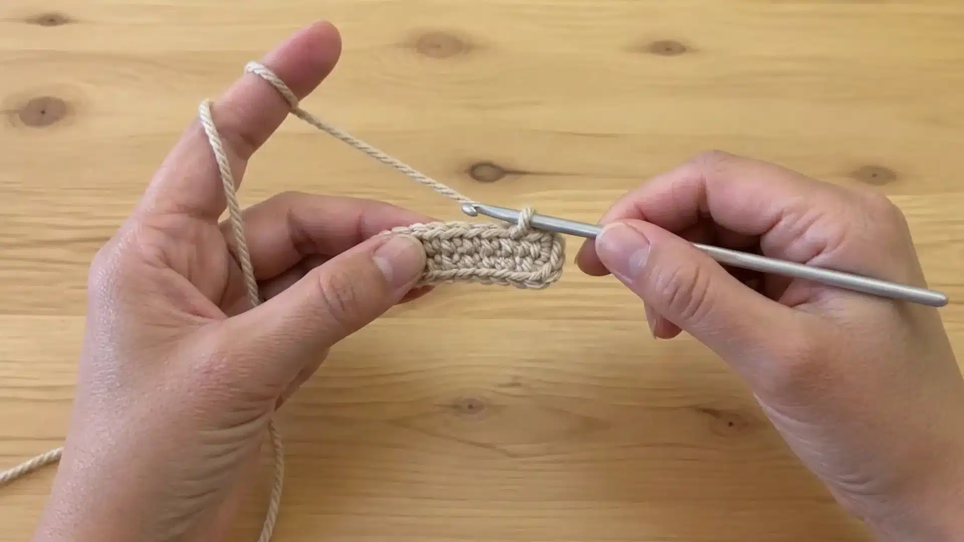 Hands holding a crochet hook and yarn while working a crochet piece