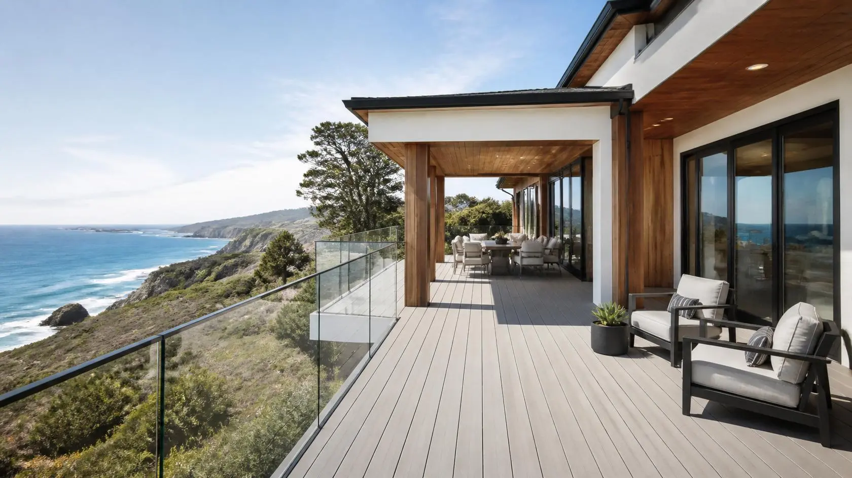 Modern beach house wrap-around deck with composite decking, glass balustrade, timber pergola, and coastal cliff views.