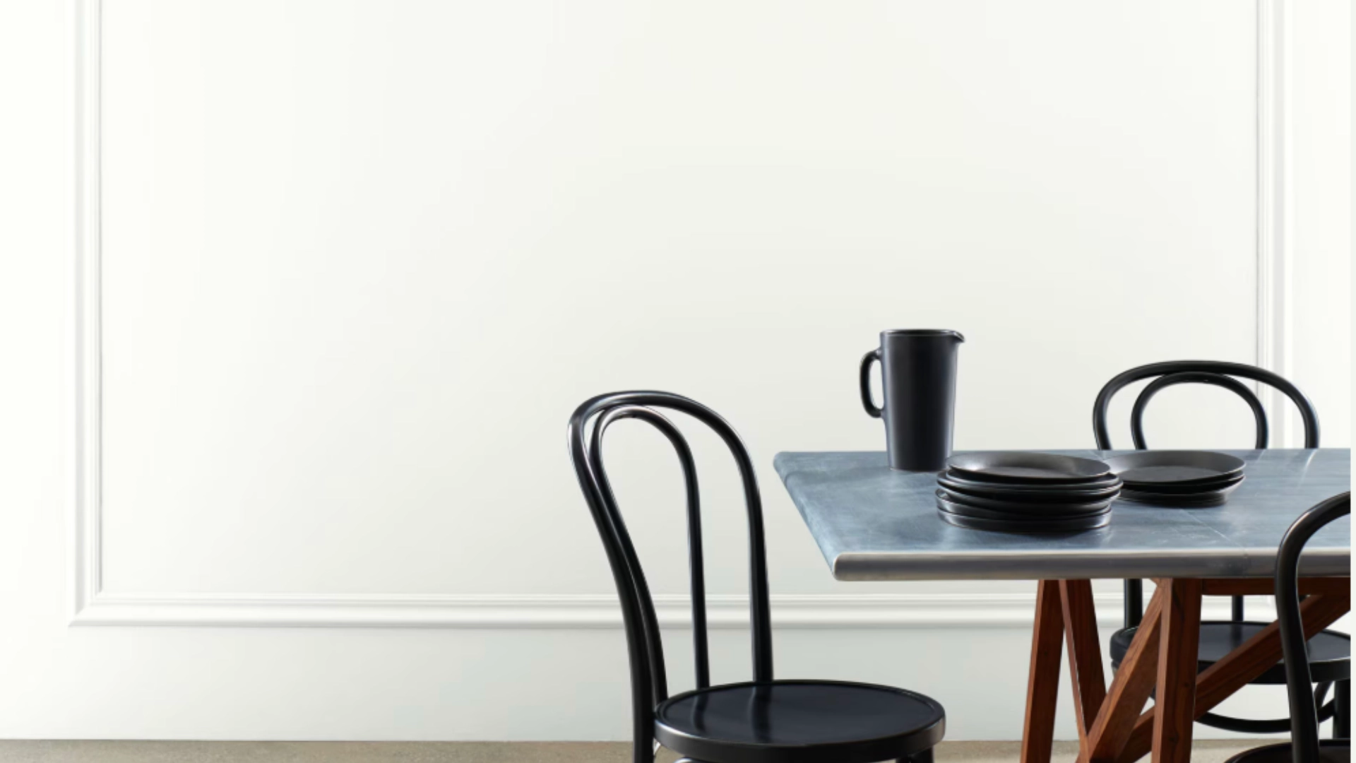 Off-white wall behind a dining table styled with black chairs and tableware