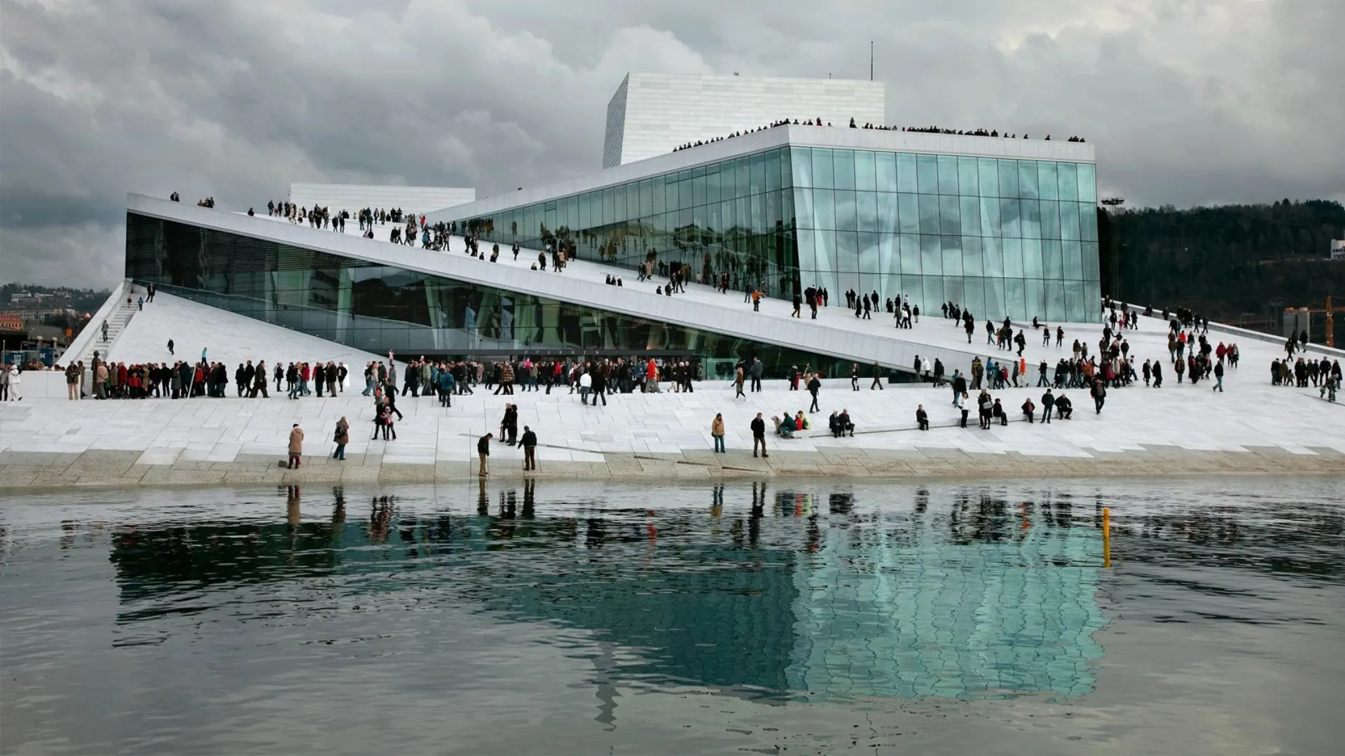 oslo opera house beside the waterfront with sloping walkable roofs reflecting in calm blue water