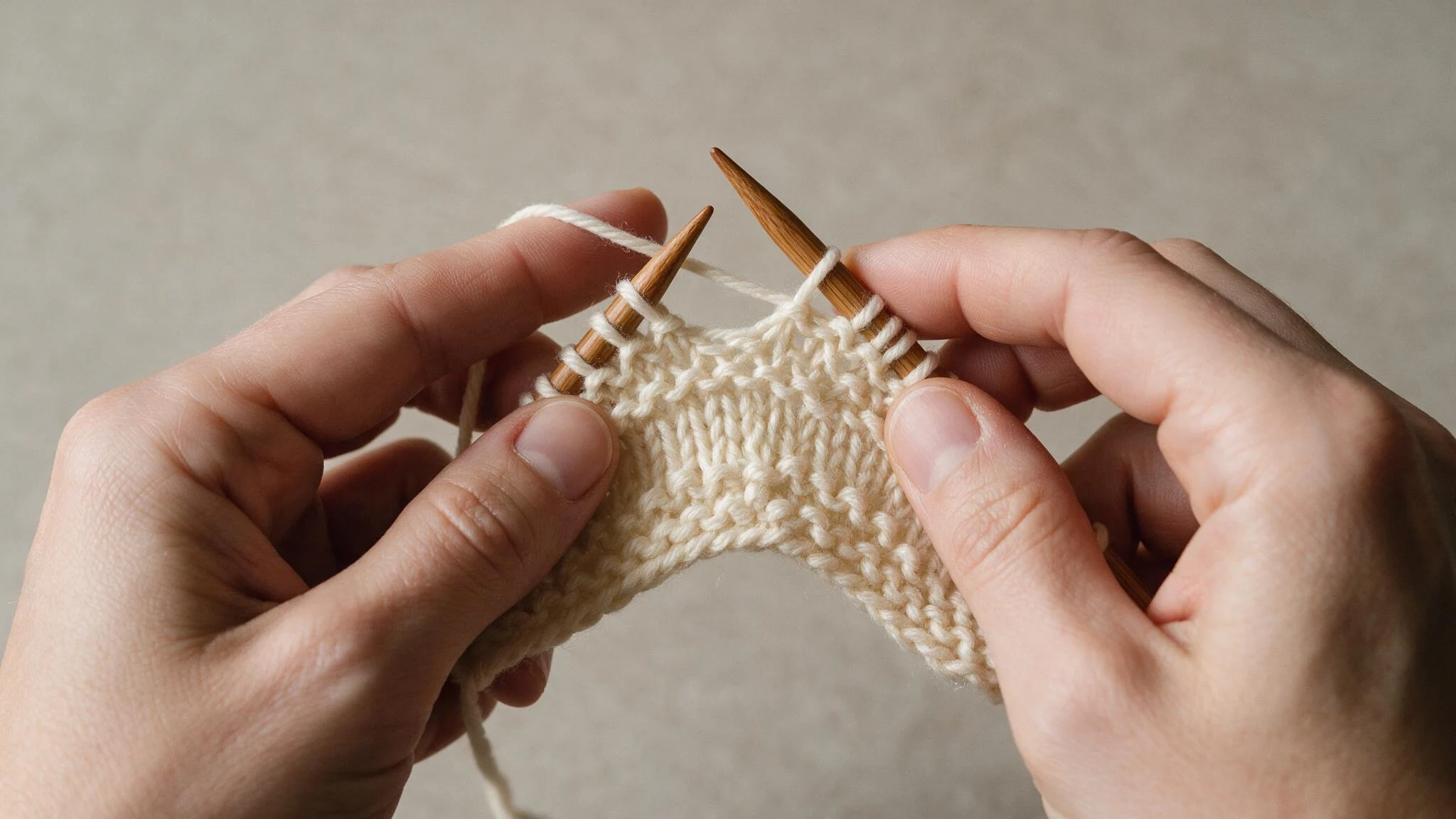 Individual knitting with needles, working on a cream yarn project, showcasing their skill and concentration.