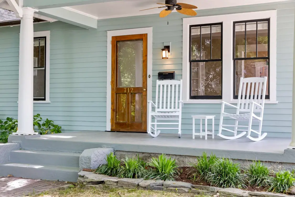 Rustic wooden porch with white rocking chairs and light blue siding in natural daylight