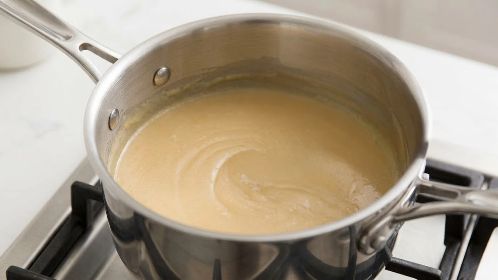 Smooth blond roux stirring with a wire whisk in a stainless steel pot on a stove