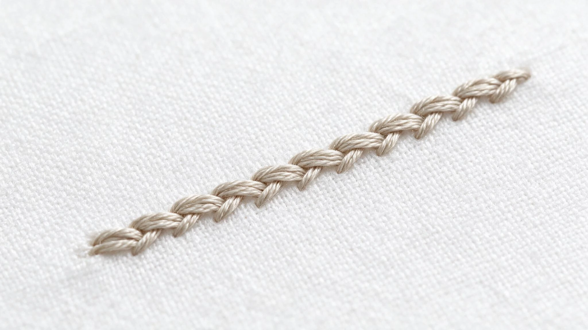 Split stitch in beige thread forming a neat connected textured line across white fabric in a simple embroidery sample