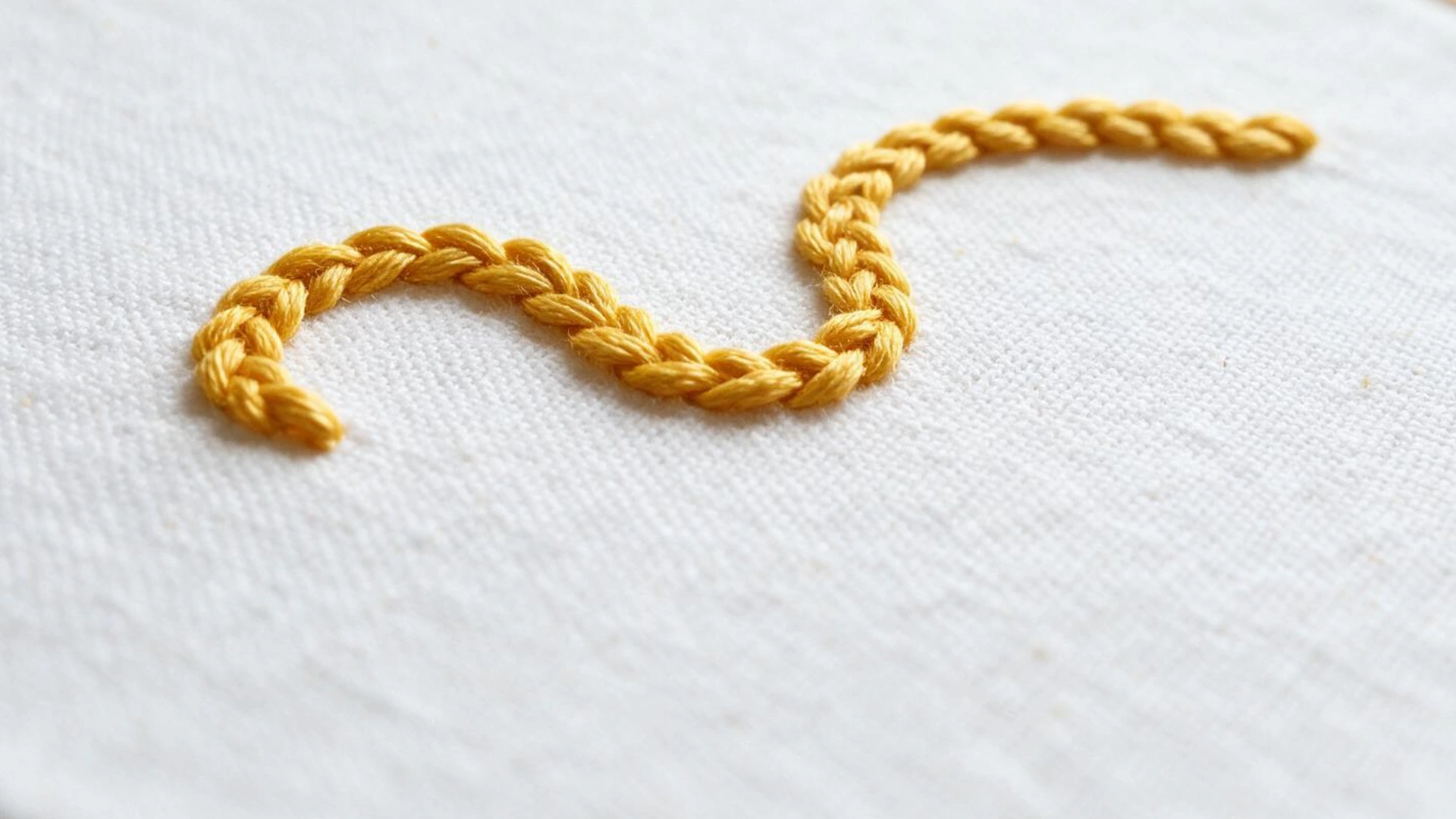 Stem stitch in golden thread forming a gently curved rope like line across white fabric in a simple embroidery sample